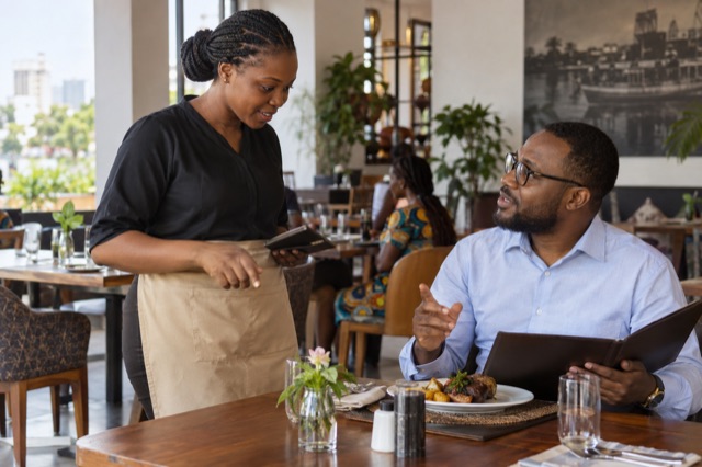 Illustration d’une serveuse échangeant avec un client dans un restaurant en RDC.