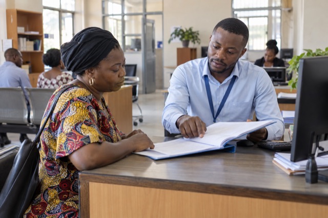 Illustration d’un agent de guichet accompagnant une usagère dans un service public en RDC.